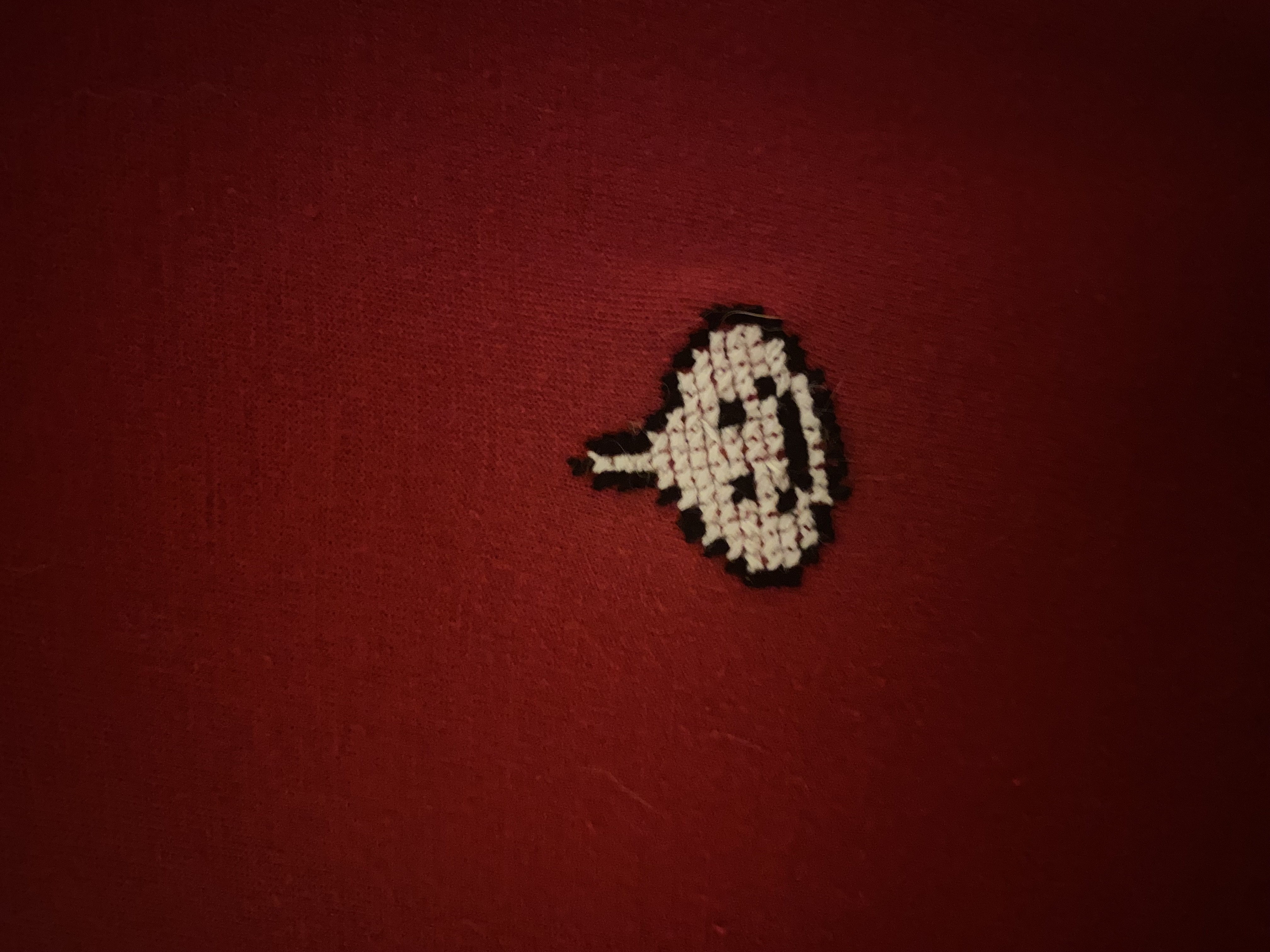 cross stitch of a white and black dragon quest slime on a red shirt